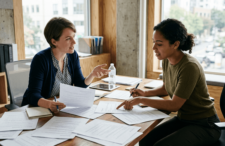 Deux collègues révisant des documents de candidature sur une table de bureau